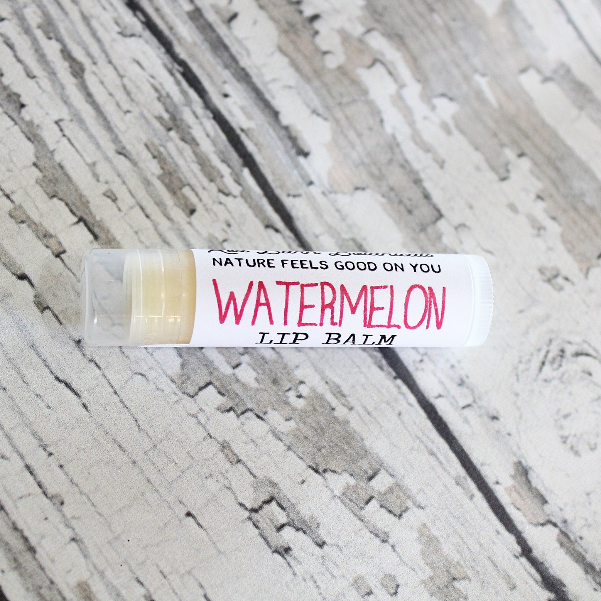 Watermelon lip balm tube with white and pink text, clear cap, on textured surface