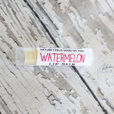 Watermelon lip balm tube with white and pink text, clear cap, on textured surface