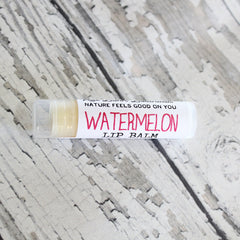 Watermelon lip balm tube with white and pink text, clear cap, on textured surface