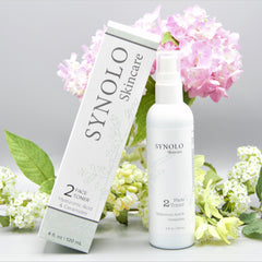 Face toner bottle and box with white and green text, white background, and flowers