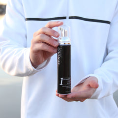 Foaming face wash bottle, black and silver, held in hands, SYNOLO brand visible