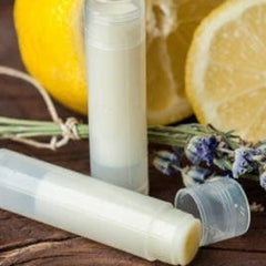 Lip balm tubes with white and clear plastic, yellow balm, and lemon slices on wood surface