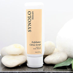 Citrus scrub bottle with white and tan label, Synolo skincare brand, and white stones displayed