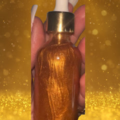 Close-up of 24K gold shimmering body oil bottle tilted to showcase golden liquid texture and sleek black pump