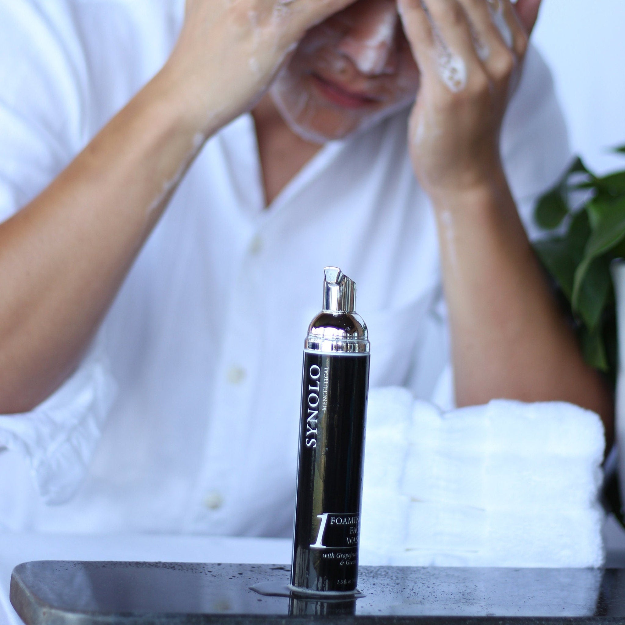 Facial cleanser bottle with black and silver design, white foam on face, and white shirt visible