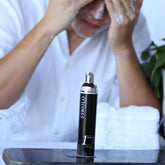 Facial cleanser bottle with black and silver design, white foam on face, and white shirt visible