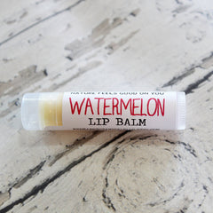 Watermelon lip balm tube with white label and red text, on a textured surface.
