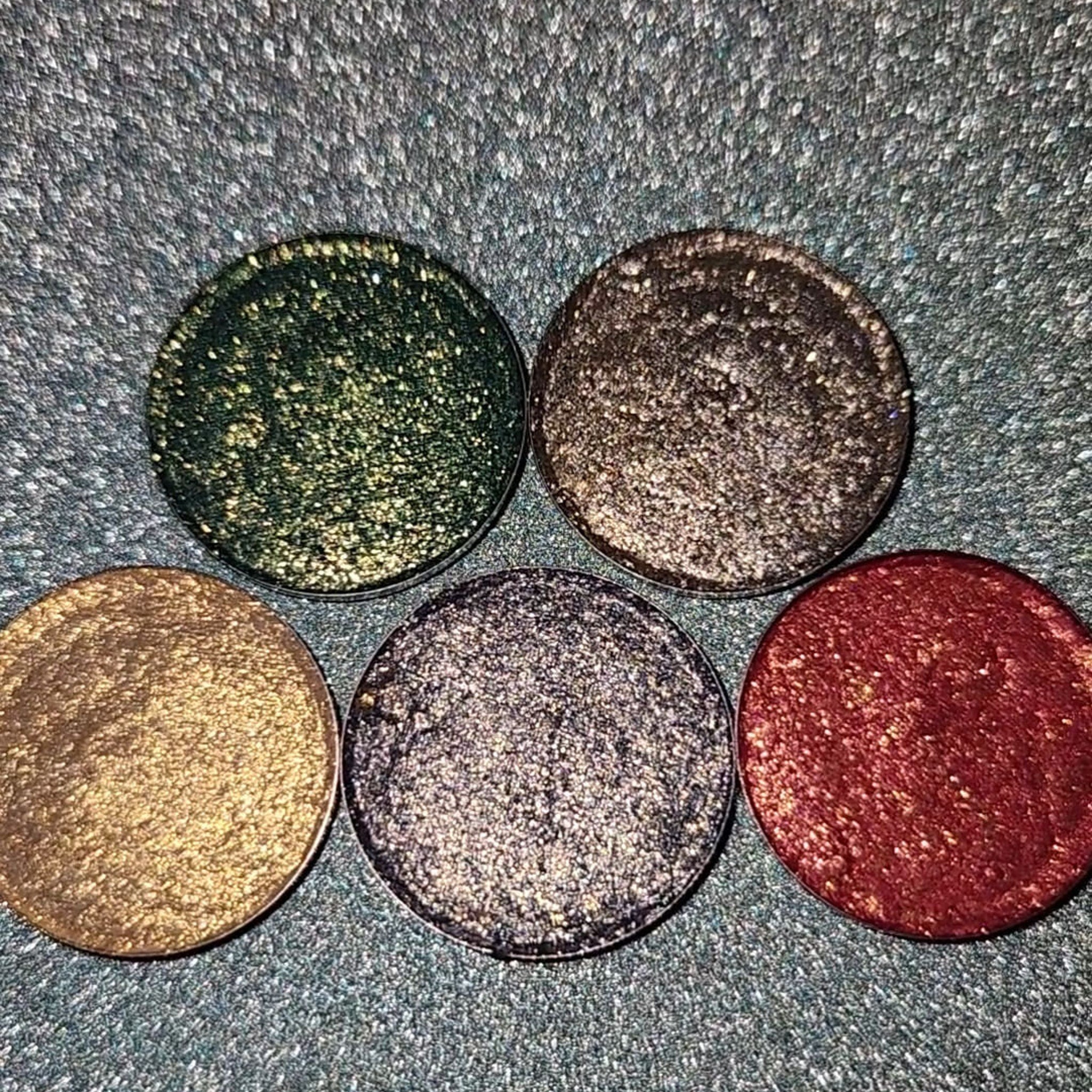 Close-up of Holiday Sparklers Eye Shadow palette with shimmering gold, emerald, and ruby shades in sleek black compact