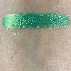 Close-up of fingertips applying shimmering fir green eyeshadow to eyelid with soft blending brush