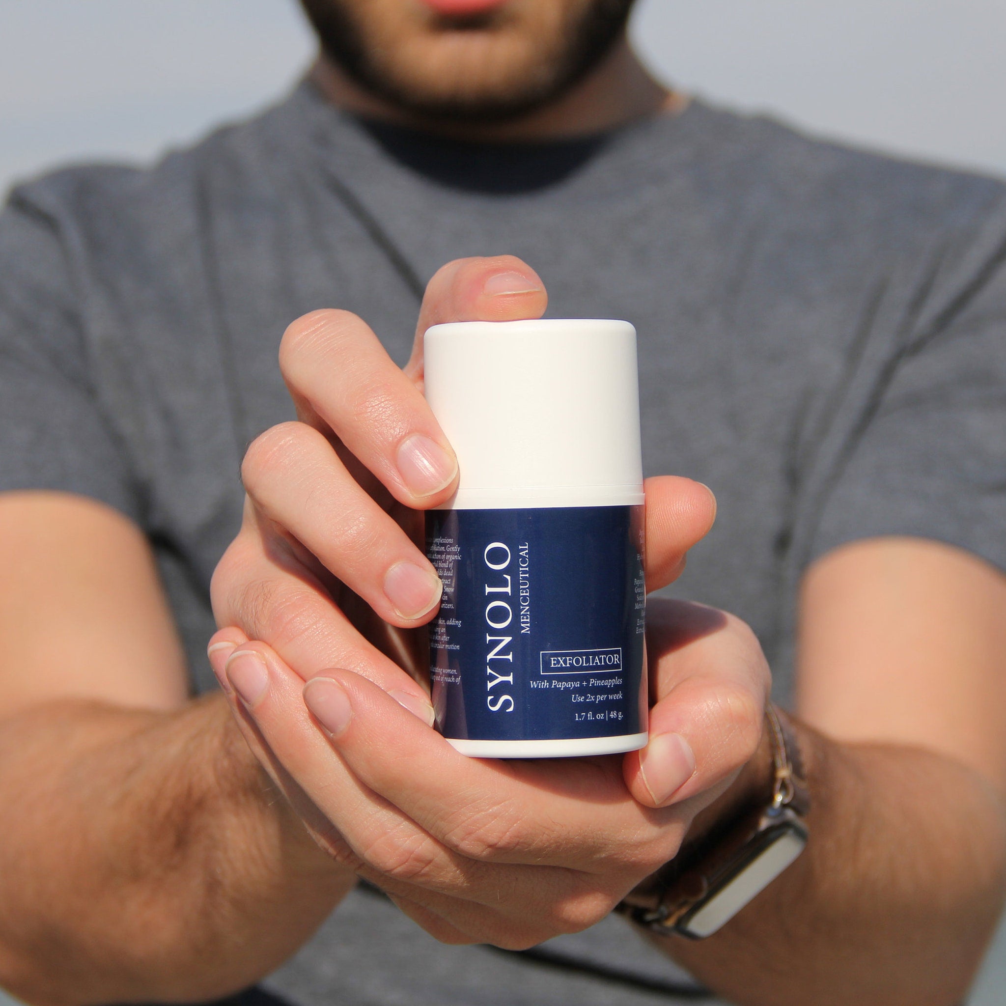 Facial Cleanser product, white and blue cylindrical container held in hands, Synolo Menceutical brand visible