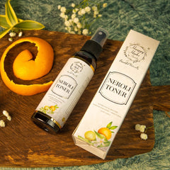 Neroli toner bottle with black cap and white label, next to a box with brand name and orange illustration on a wooden surface