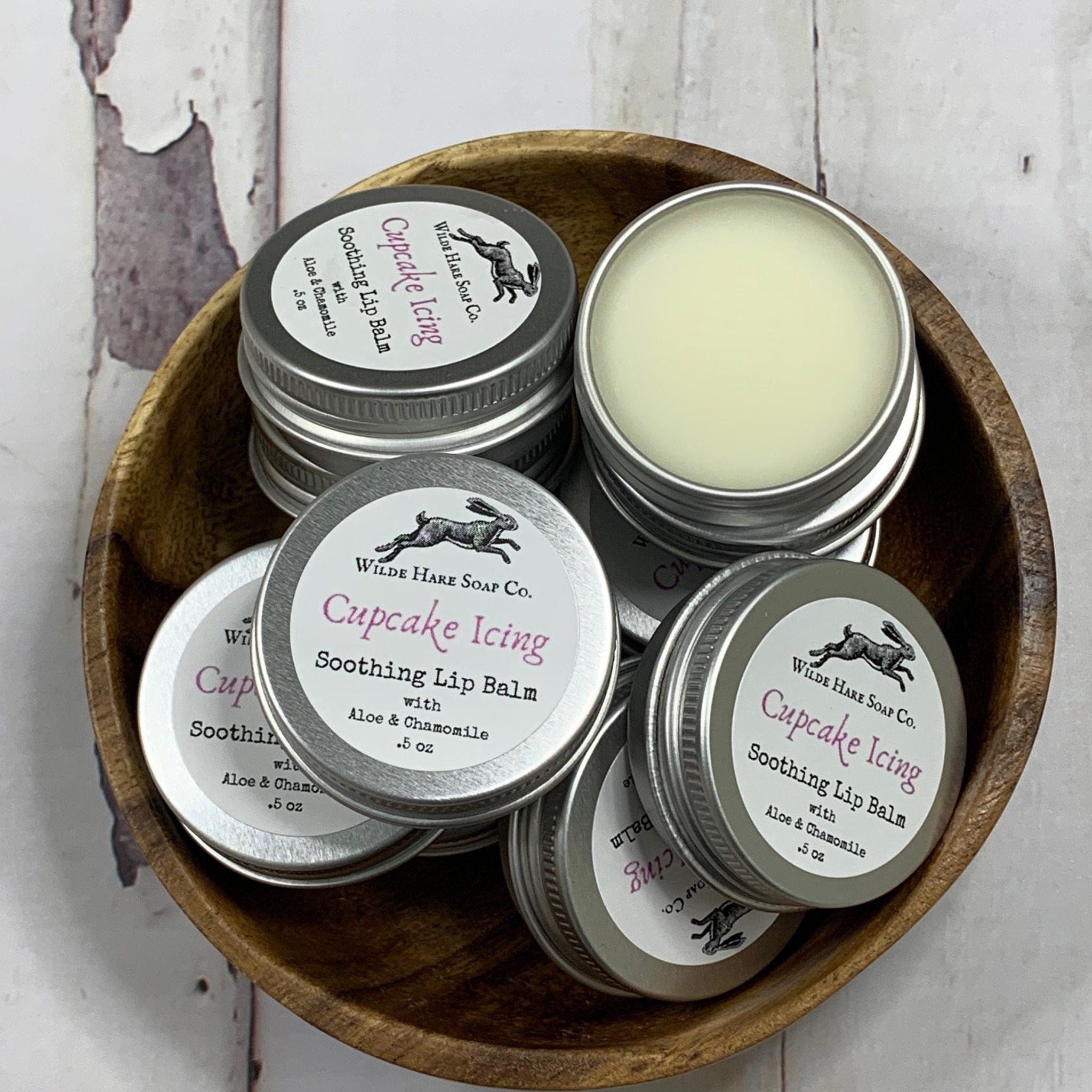 Lip balm tins, silver metal containers, Wilde Hare Soap Co. branding, wooden bowl