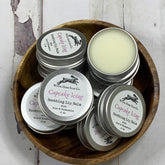Lip balm tins, silver metal containers, Wilde Hare Soap Co. branding, wooden bowl