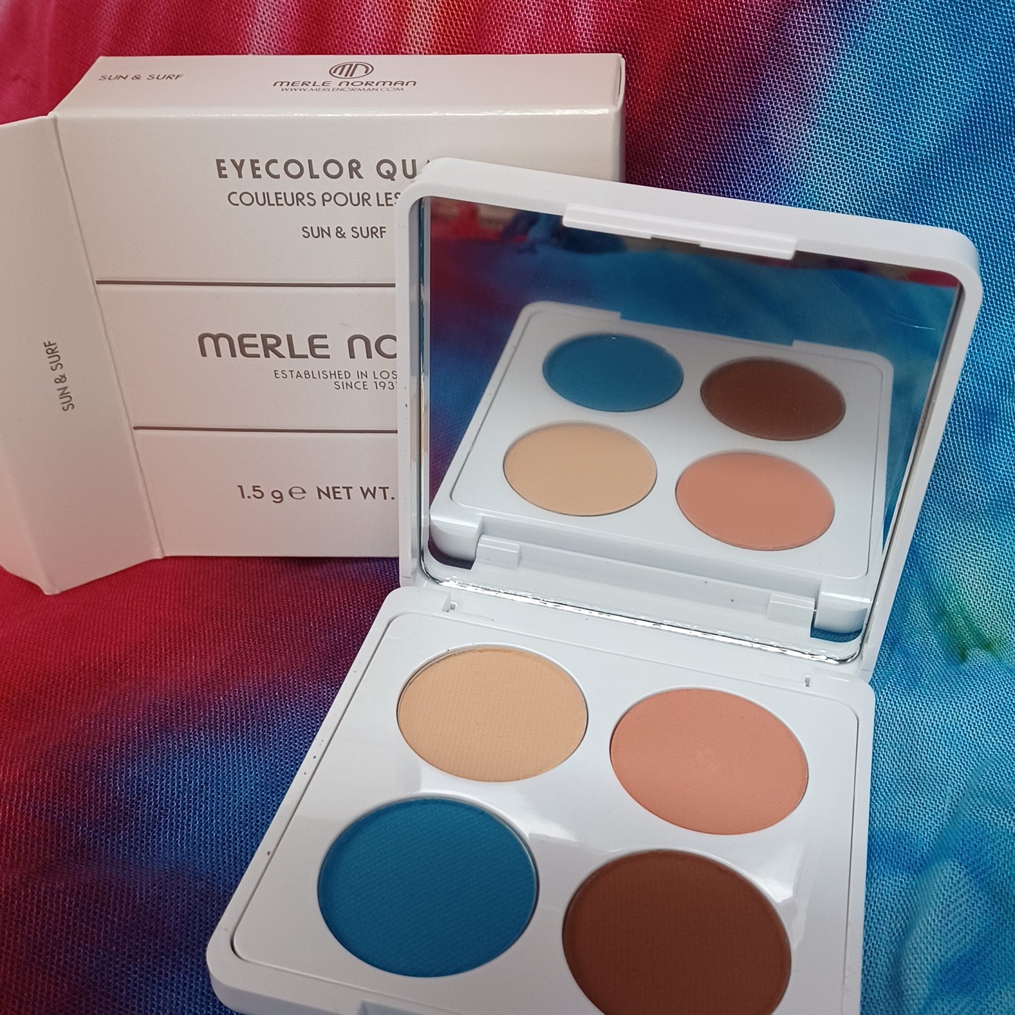 Eye shadow palette with white case and Merle Norman text, containing blue, peach, and brown colors, open for display