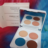 Eye shadow palette with white case and Merle Norman text, containing blue, peach, and brown colors, open for display