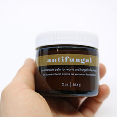 Antifungal balm jar, brown and gold label, white lid, held in hand, GLEAM & GLOW text visible