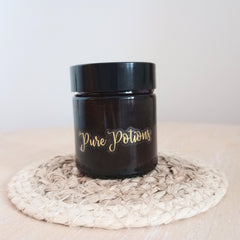 Dark glass jar with gold "Pure Potions" label on woven coaster