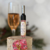 Champagne lip gloss in a bottle with silver cap, on wood, next to a gift