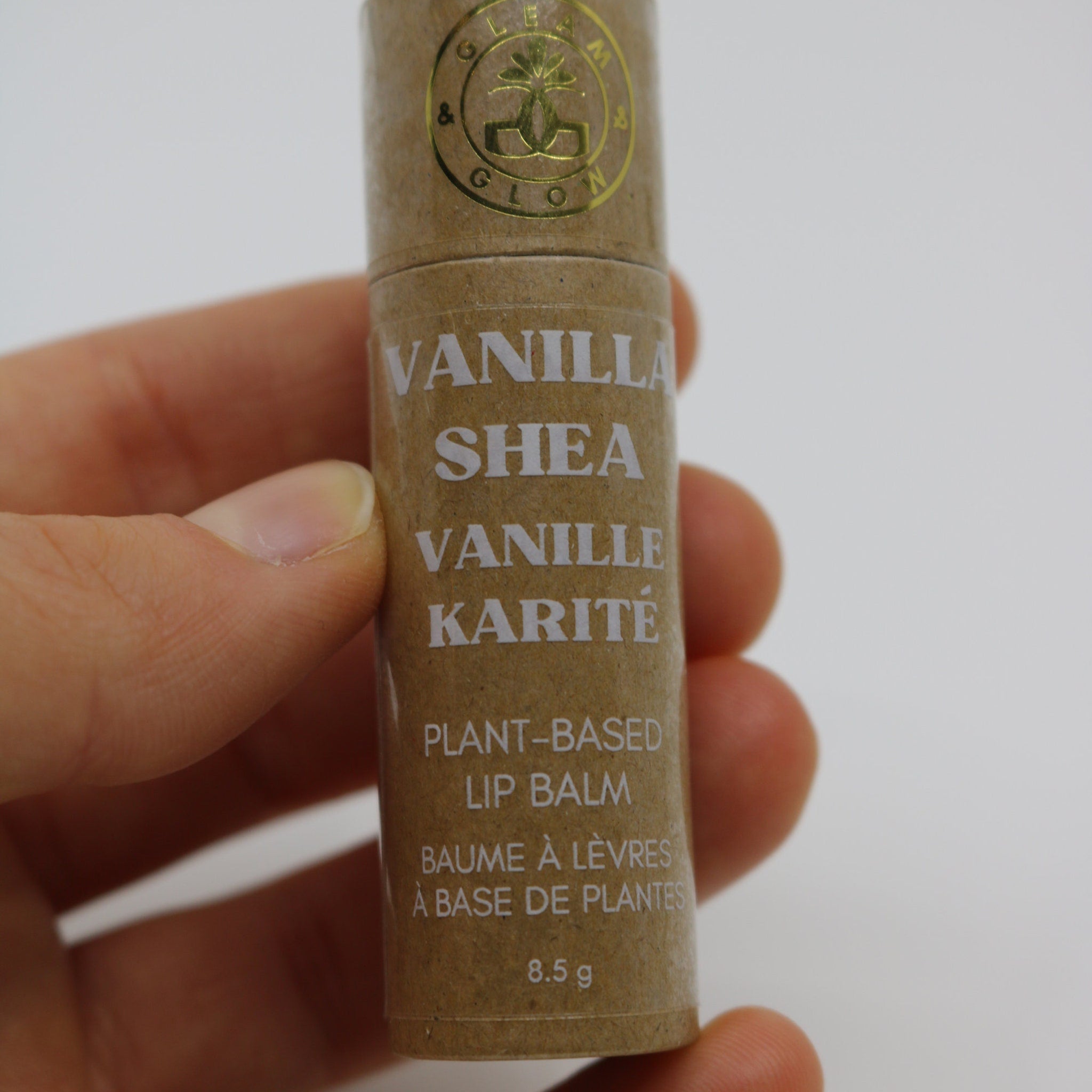 Lip balm tube in brown cardboard with white text, held in hand, GLEAM & GLOW logo visible