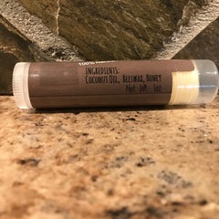 Lip balm tube with brown label, clear plastic, and white cap, ingredients visible