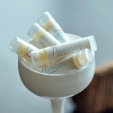 Lip balms in white tubes with clear caps, inside white bowl, Linger brand