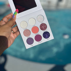Eyeshadow palette with white case, various colors, and mirror held in hand near pool