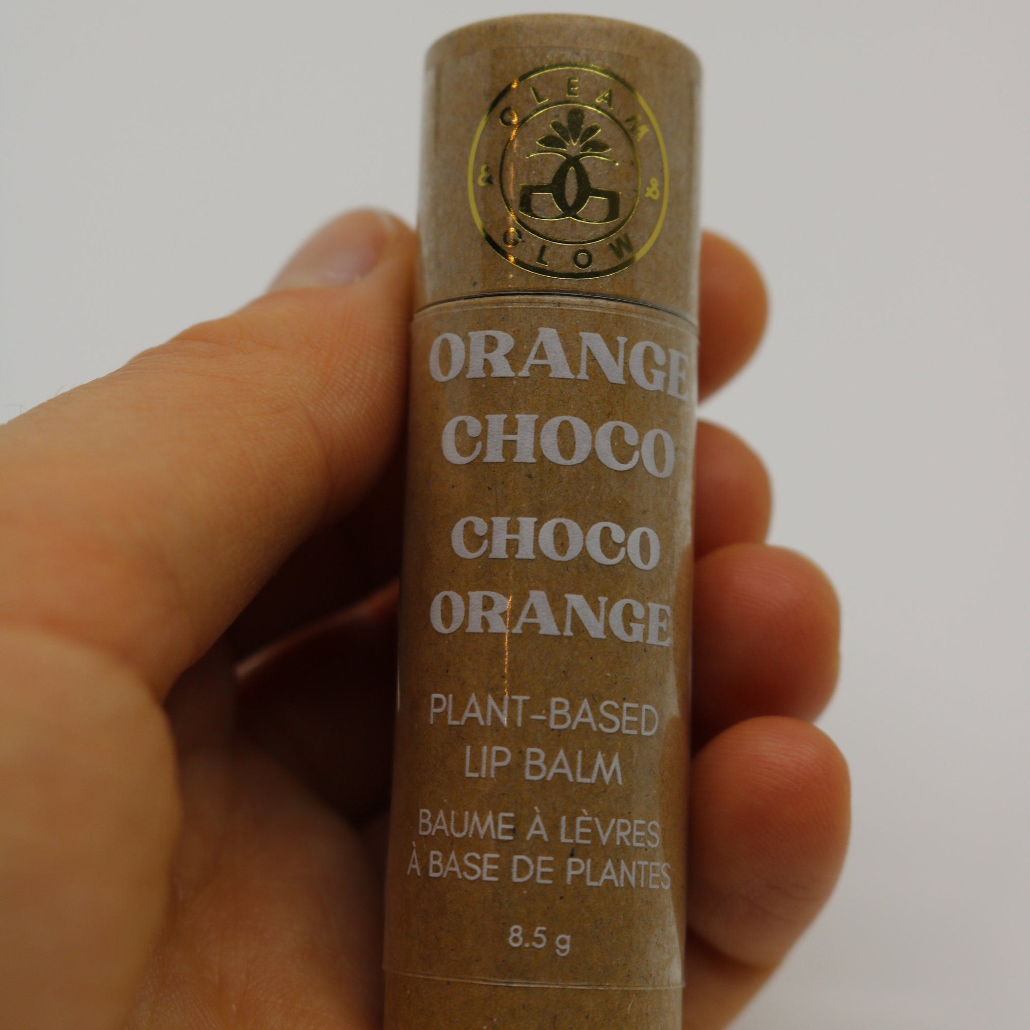 Lip balm tube in brown with white text, held by hand, GLEAM & GLOW logo visible