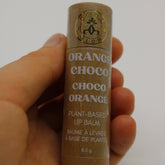 Lip balm tube in brown with white text, held by hand, GLEAM & GLOW logo visible