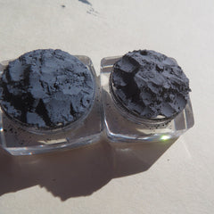 Gray powder in clear square containers, rough texture, on light surface