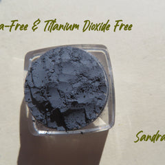 Powdered dark gray product in clear square container, textured surface, Sandra text