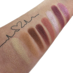 Eyeshadow swatches with various shades of brown, pink, and gold on skin, with heart tattoo detail