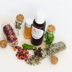 Glass bottles with corks, dried herbs, and a brown liquid with a white lid, on white surface.