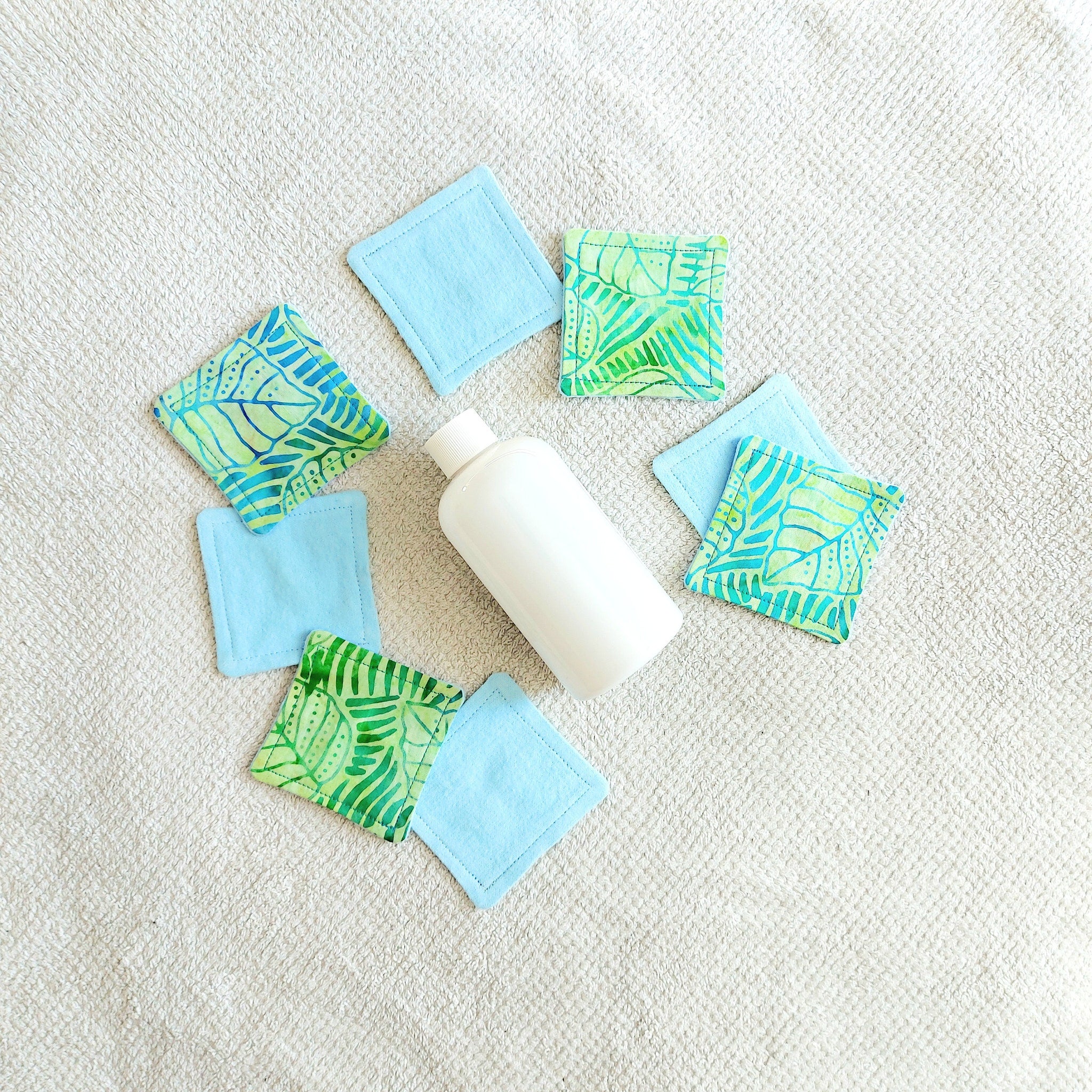 Makeup remover pads, blue and tropical print fabric, arranged with lotion bottle on white towel