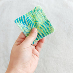 Reusable facial pad with blue and green patterned fabric, held in hand