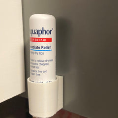 Lip repair product in white tube with red and blue text, held in a white holder, Aquaphor brand visible