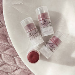 Tinted lip balm in clear tubes with burgundy balm, "elderberry" label, on white surface