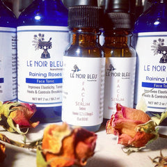 Face serum and tonic bottles, brown and blue glass, white labels with brand text and dried roses