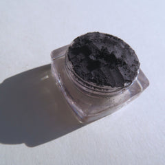 Black powder in clear glass jar with visible shadow on white surface