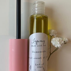 Lash oil bottle with clear glass, pink applicator, and white label with text and flowers