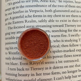 Eye shadow, reddish-brown powder in a clear container, on a book page