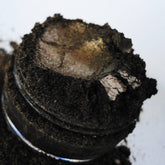 Dark brown eyeshadow with metallic shimmer, in a glass jar, close-up view