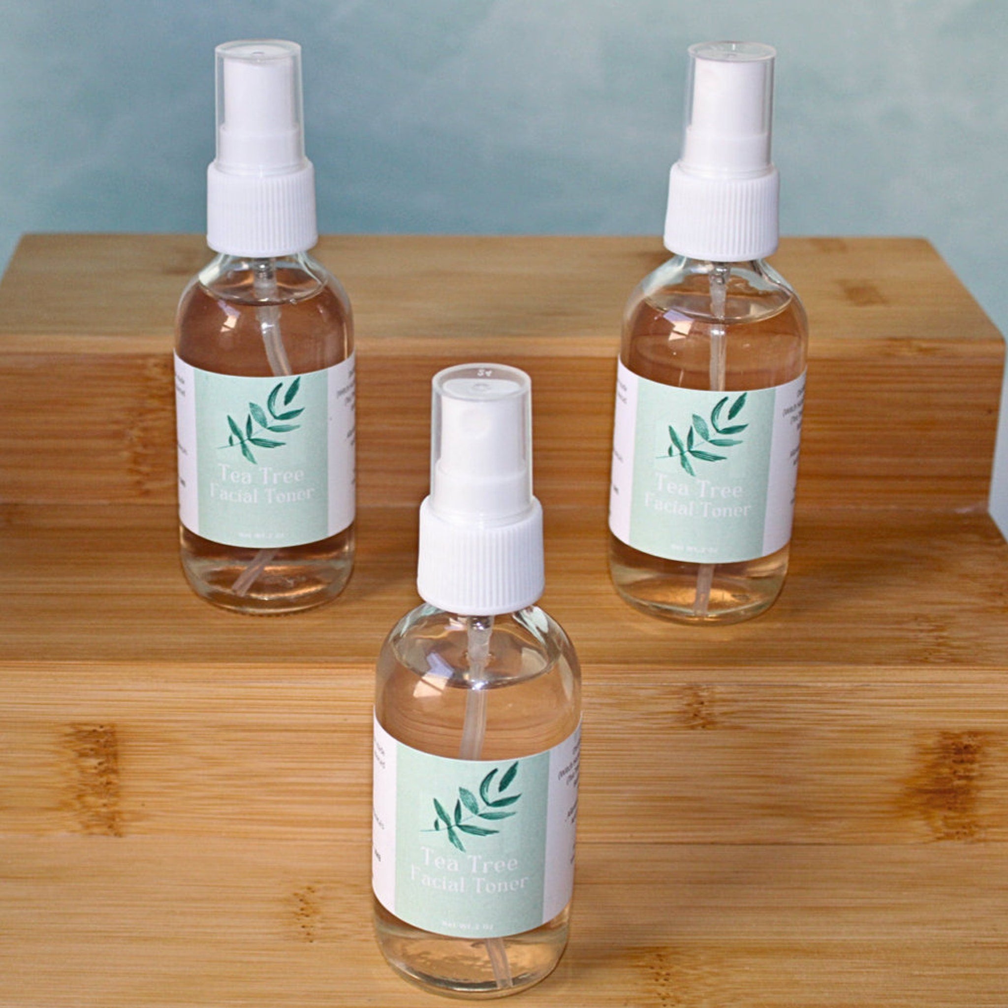 Facial toner bottles, clear glass with white spray tops, on wooden surface, JM Botanicals label visible