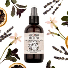 Facial cleanser bottle with Wild Rose label, brown glass, and clear pump top surrounded by botanicals