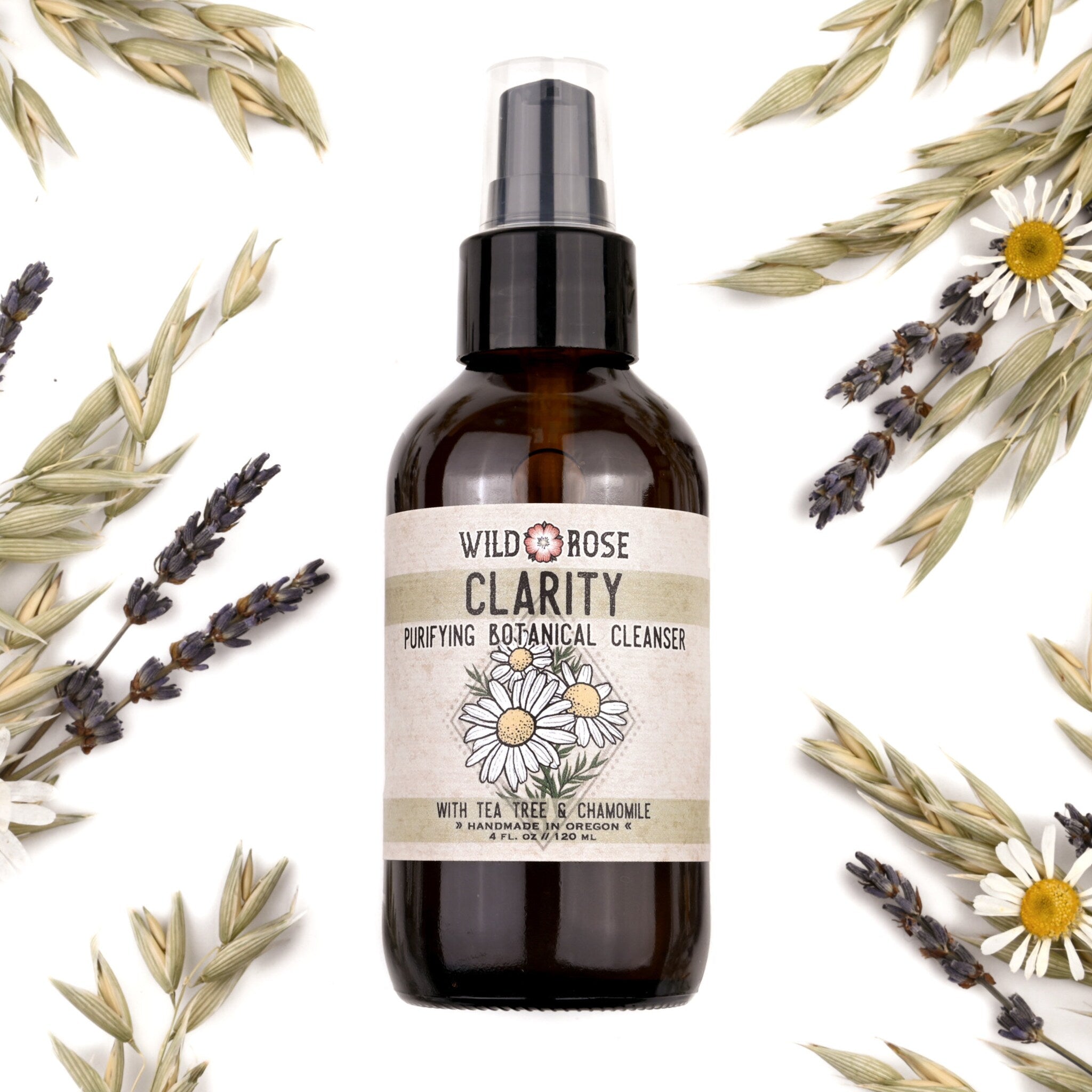 Facial cleanser bottle, brown glass with pump, Wild Rose Clarity label, surrounded by botanicals