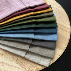 Linen fabric swatches in various colors, stacked on a wooden surface, showing texture and color variations