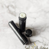 Lip balm in black tube with white balm visible, SOLETLUNA logo on surface