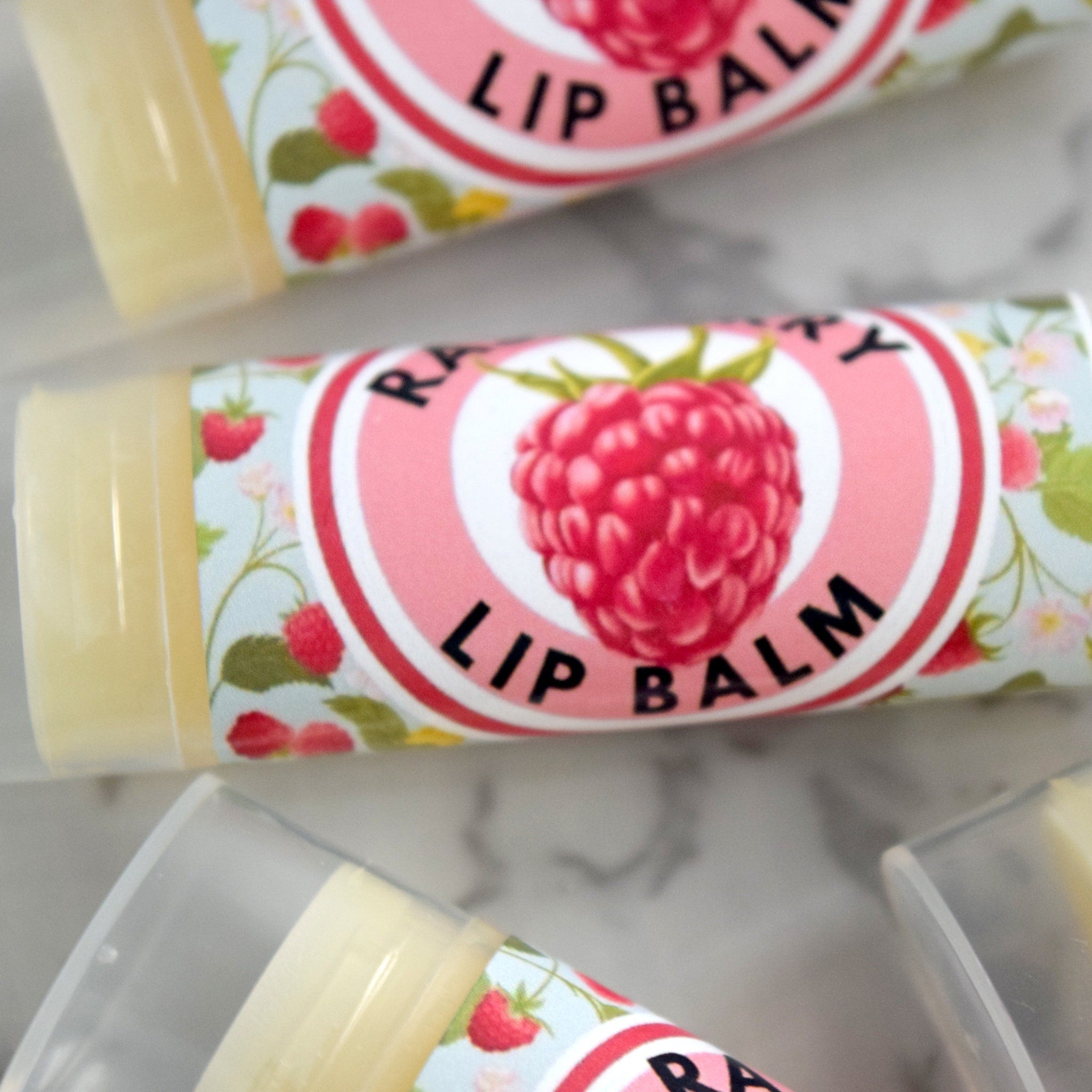 Lip balm tubes with floral pattern, pink and white label, and raspberry graphic
