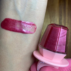 Lip gloss swatch with pink shimmer and diamond-shaped container on skin, showing color and texture