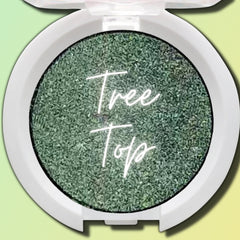Close-up of a makeup brush applying vegan pressed eyeshadow in a compact pan, showing smooth pigment blend.
