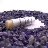 Vegan lip balm tube with white label, yellow balm, and Aura Light Apothecary text, surrounded by purple stones